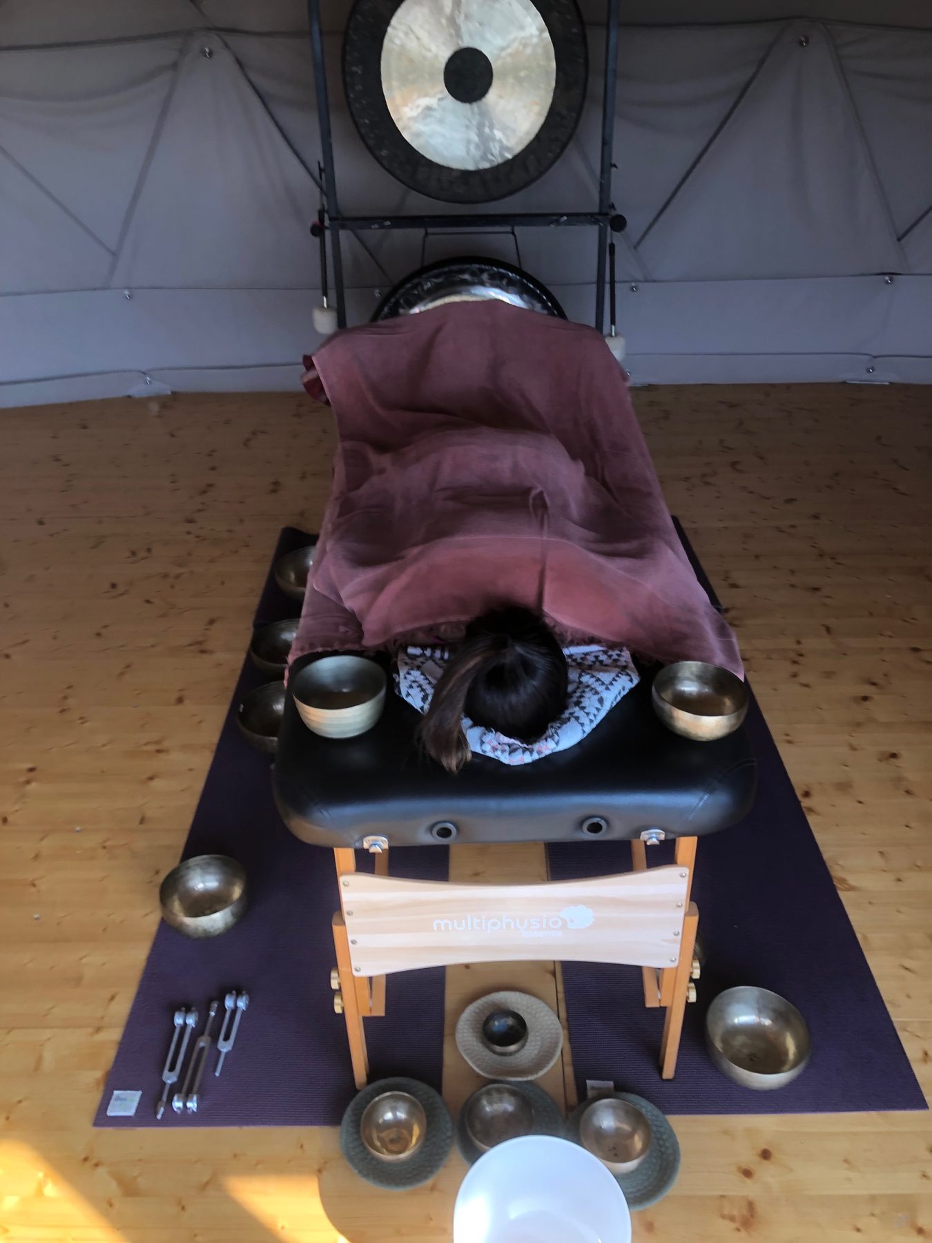 Person resting on a massage table surrounded by singing bowls and a gong